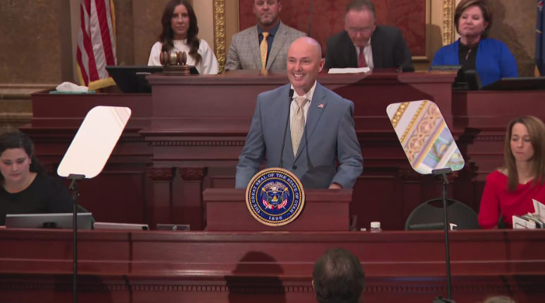 a man speaking in a suit, bald and smiling...